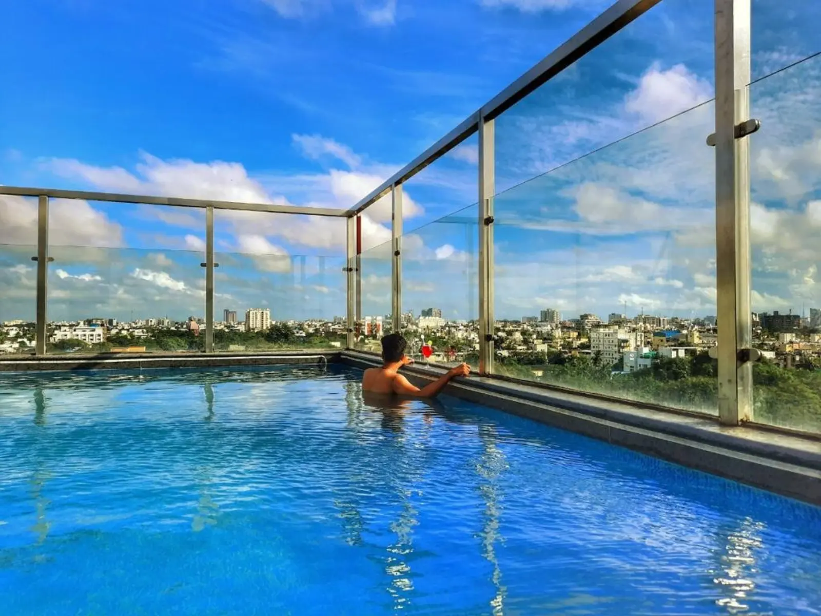 Glass-fenced rooftop infinity pool overlooking the city skyline — CreativPools